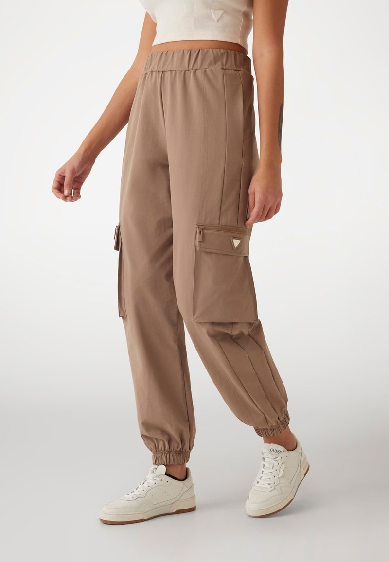 Bruine cargobroek met elastische tailleband, zijzakken en gathered cuffs. Gecombineerd met witte sneakers voor een casual uitstraling.
