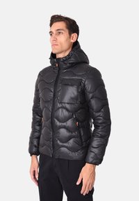 Giubbotto imbottito nero con un motivo a trapuntatura ondulata, zip frontale e tasche, e cappuccio. Presenta dei tiranti della zip arancioni a contrasto.