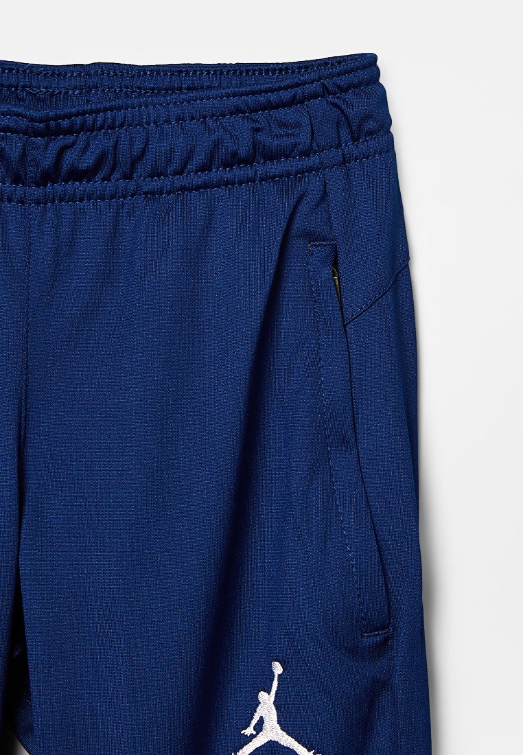 Pantalon de sport bleu avec une taille élastique, poche zippée latérale et logo Jordan blanc brodé en bas à gauche. Texture lisse.