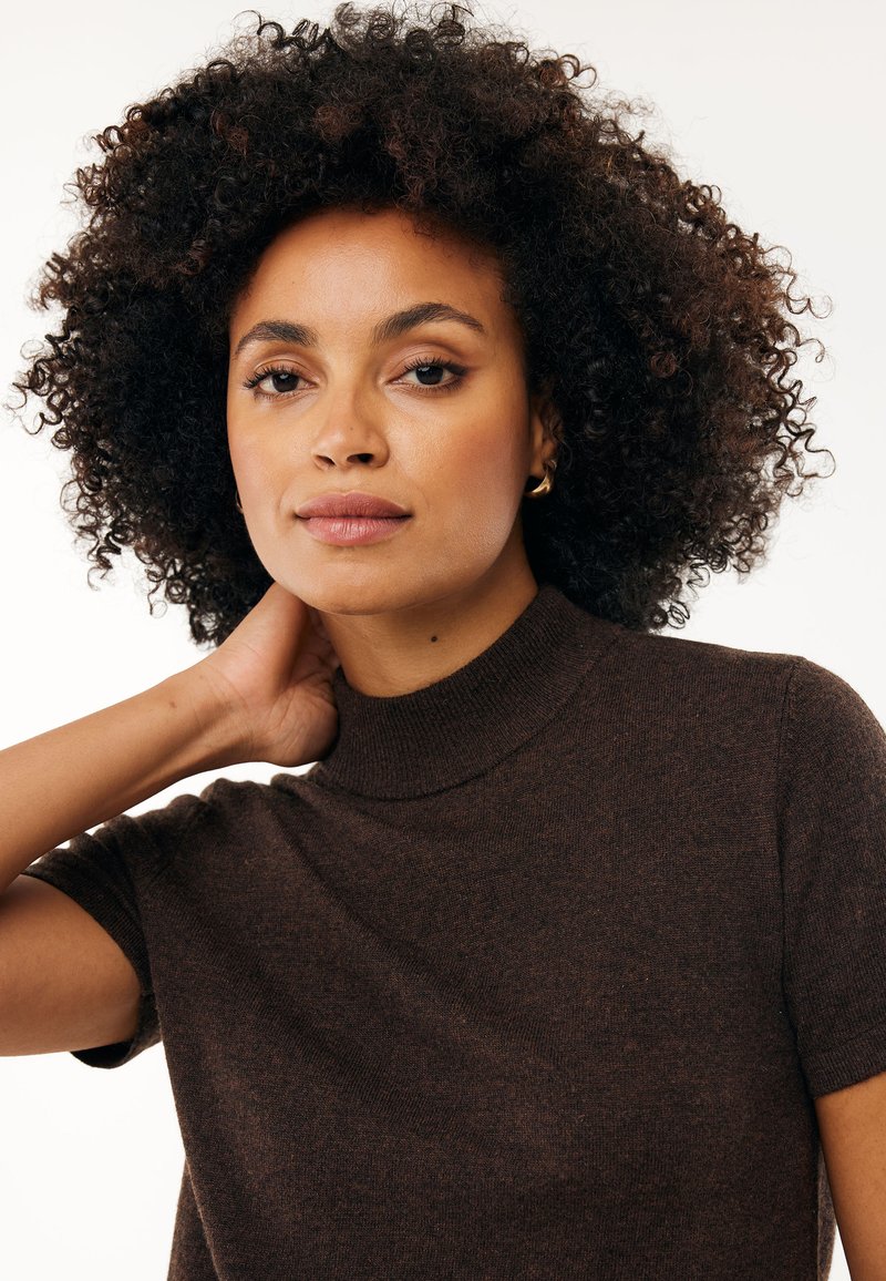 Brązowy dzianinowy top z wysokim dekoltem i krótkimi rękawami, o gładkiej teksturze i subtelnych odcieniach koloru.