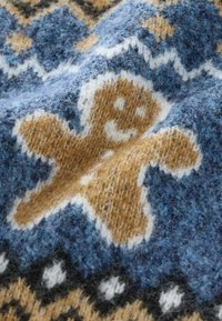 Muster eines braunen Lebkuchenmanns, das in blauen Wollstoff mit weißem und schwarzem dekorativem Saum gestrickt ist.
