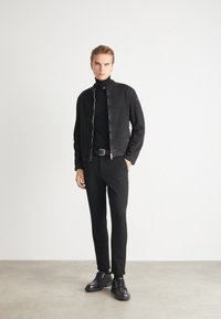 Black denim jacket with a zip closure, paired with a black turtleneck, slim black pants, and black leather shoes. Smooth texture, minimalist design.