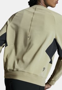 Beige sweatshirt met zwarte accenten, textuurstof, een ronde hals en een zichtbare naad aan de achterkant, ideaal voor sportkleding.