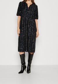 Svart paljetterad midiklänning med vertikala ränder, korta ärmar och V-ringning. Matchas med glänsande svarta knähöga spetsiga stövlar.