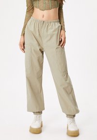 Pantalones cargo de color beige claro con cintura elástica, dos bolsillos laterales y puños elásticos. Combinados con un top corto de encaje semitransparente y botas de platform blancas.