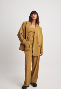 Blazer cintré jaune moutarde à un bouton, pantalon large assorti et crop top ajusté. Texture lisse, design structuré.