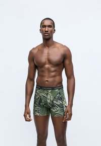 Férfi boxeralsó, fekete derékkal, amelyen a "BJÖRN BORG" márkázás található, zöld és fekete pálmalevél mintával, texturált anyagon.