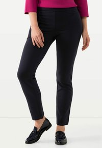 Pantalones marino de corte slim, confeccionados con una tela elástica, que presentan una textura suave y bolsillos laterales. Combinados con mocasines negros brillantes.