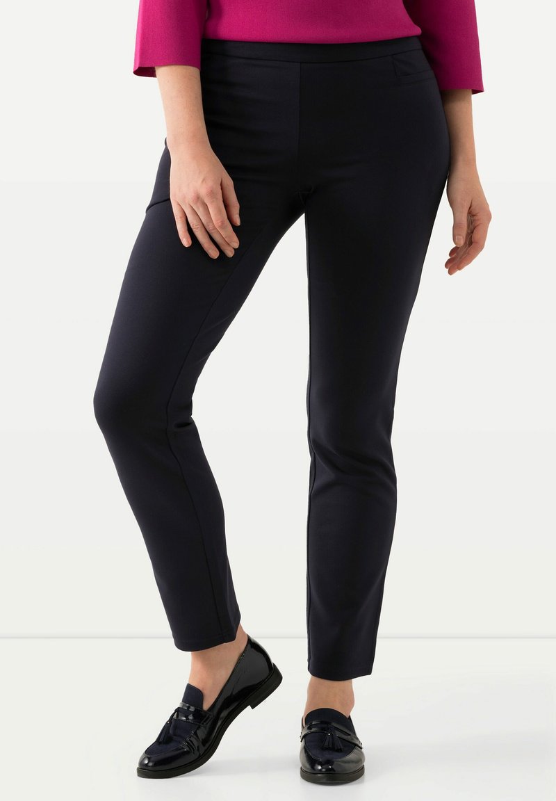 Pantalones marino de corte slim, confeccionados con una tela elástica, que presentan una textura suave y bolsillos laterales. Combinados con mocasines negros brillantes.