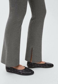Črne ravne čevlje z okroglo toe in majhnimi okraski iz rhinestones, v kombinaciji z rebrastimi sivimi pletenimi hlačami z bočnim rezom.