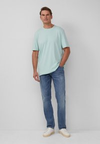 Hellblaues T-Shirt mit kurzen Ärmeln, kombiniert mit ausgewaschenen blauen Jeans und weißen Sneakers. Einfaches Design mit rundem Ausschnitt und lässiger Passform.