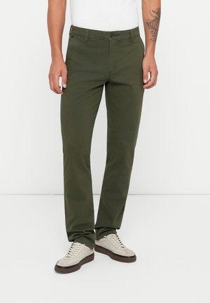 Dark green chinos made from cotton, featuring a straight leg design, front pockets, and a button closure. Worn with cream-colored sneakers.