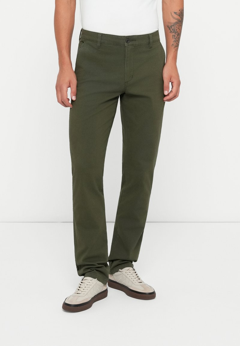 Dark green chinos made from cotton, featuring a straight leg design, front pockets, and a button closure. Worn with cream-colored sneakers.