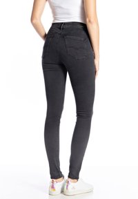 Jeans negros ajustados con una cintura alta, que cuentan con dos bolsillos traseros y una textura suave y lisa. Llevados con zapatillas blancas, que muestran acentos coloridos.