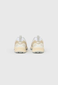 Μπεζ και λευκά αθλητικά παπούτσια με υφή στην επιφάνεια, γκρι λεπτομέρειες και θηλιά στο πίσω μέρος. Αντανακλαστικές λεπτομέρειες στα πλευρά.