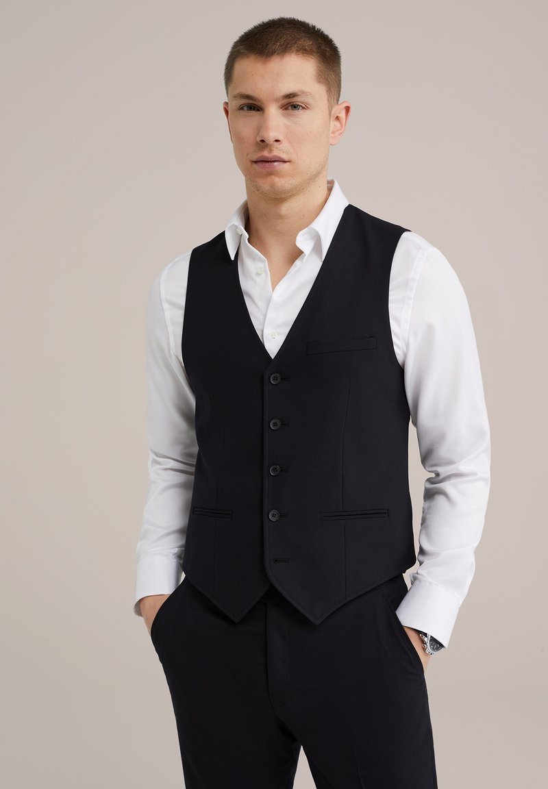 Vesta neagră cu cinci nasturi, design în formă de V, și două buzunare frontale, purtată peste o cămașă albă. Textură de țesătură netedă cu un croi ajustat.