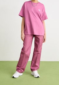 Roze katoenen t-shirt met een relaxte pasvorm en een klein logo op de borst, gecombineerd met bijpassende roze broek en witte sneakers.