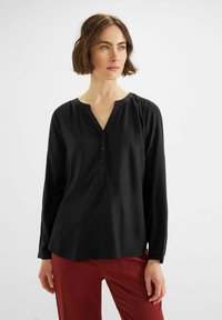 Blusa nera a maniche lunghe con scollatura a V, chiusura con bottoni e dettagli arricciati sulle spalle; tessuto leggero e morbido.