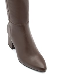 Brązowy skórzany botek za kostkę z wydłużonym noskiem, teksturowanym wykończeniem i blokowym obcasem. Posiada subtelną szew na górze.