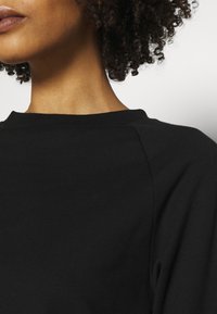 Felpa nera in cotone con scollo rotondo e maniche a raglan. Texture liscia con dettagli minimi nelle cuciture.