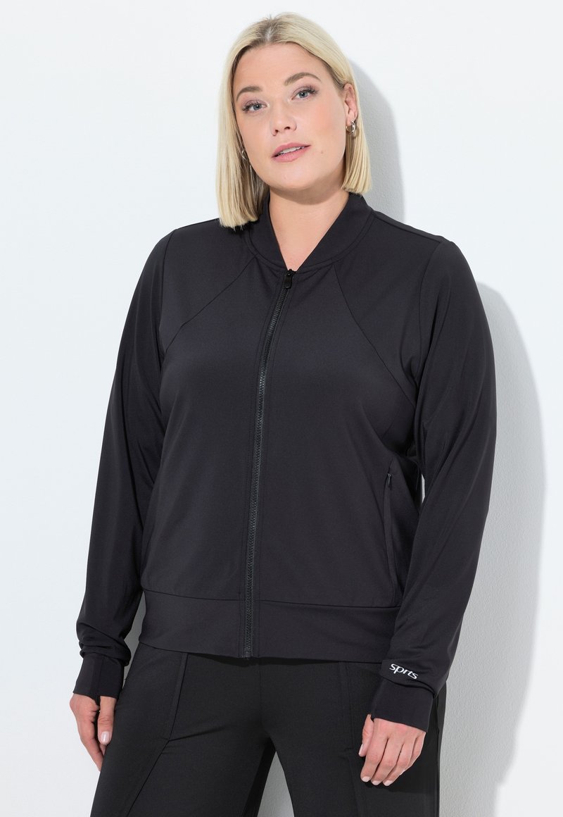 Giacca sportiva nera con zip frontale, maniche lunghe, spalle raglan e polsini con un piccolo logo sul polsino sinistro.