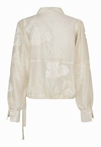 Blouse longue à manches longues en crêpe crème avec broderie florale, manches bouffantes, col, boutons aux poignets et cordon de serrage à l’ourlet.
