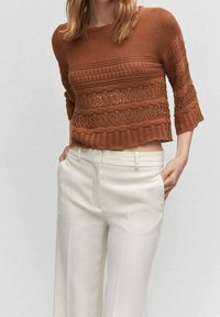 Maglione corto marrone lavorato a maglia con un design testurizzato, caratterizzato da motivi traforati e maniche tre quarti, abbinato a pantaloni bianchi a gamba larga.