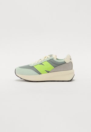 Low-Top-Sneaker in Hellgrün, grauem Mesh, neon-gelbem "N"-Logo, cremefarbener Sohle und Schnürsenkeln, vor weißem Hintergrund dargestellt.