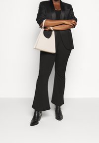 Czarna marynarka z satynowymi klapami, czarny prążkowany top, rozszerzane czarne spodnie oraz jasnobeżowa torebka o teksturowanym wykończeniu i zakrzywionym uchwycie.
