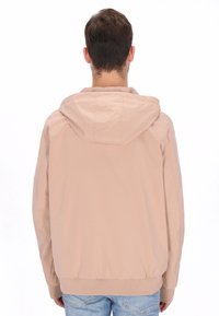 Lysebeige hættejakke i glat stof. Har en afslappet pasform, elastiske manchetter og taljebånd. Ingen synlige logoer eller mønstre.