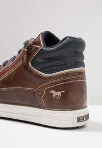 Brown leather high-top sneaker with navy accents, side zipper, red stitching, and embossed horse logo near the heel, featuring a white sole.