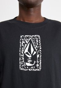 Camiseta de algodón negra con un diseño gráfico distintivo en blanco de una cara dentro de un borde rectangular, que exhibe elementos geométricos llamativos.