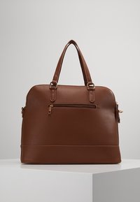 Brown leather handbag with a structured shape, double handles, and a zippered front pocket. Gold hardware accents enhance the design.