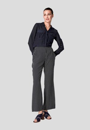 Navy Hemd mit Knöpfen und zwei Fronttaschen, kombiniert mit hoch taillierten, schwarz-weißen gestreiften weiten Hosen und dunklen Sandalen mit Blockabsatz.