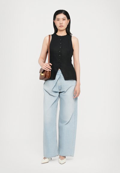 Black sleeveless top with button front, paired with loose light blue denim trousers and white pointed-toe shoes, holding a brown crossbody bag.