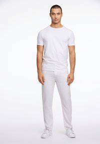 Camiseta blanca de algodón de cuello redondo combinada con pantalones de lino texturizados en gris claro y zapatillas blancas, con un ajuste relajado y un diseño sencillo.