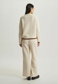 Pull en crème à côtes avec une ceinture marron, associé à un pantalon évasé beige. Texture lisse, coupe décontractée et design simple.