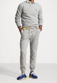 Grå sweatshirt med rund halsringning och logotyp, tillsammans med matchande grå sweatpants med dragsko i midjan. Avslutas med blå och gula sneakers.