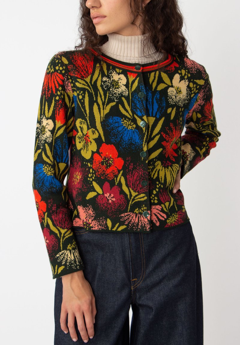 Cardigan fleuri avec un fond vert foncé, orné de fleurs rouges, bleues et roses. Texture en tricot, col rond et boutons verts.