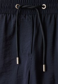 Pantalons avec taille élastique bleu marine, dotés d'un cordon de serrage, mettant en avant des accents en métal doré brillant et un tissu lisse légèrement brillant.