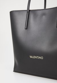 Zwarte leren tote bag met twee handvatten, met een gladde afwerking en het gouden "Valentino" logo aan de voorkant.