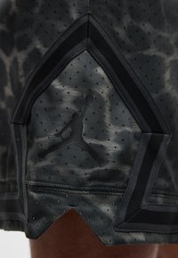 Czarne krótkie spodenki sportowe z perforowaną tkaniną, ciemnym wzorem tie-dye oraz czarnym logo Jumpman w kształcie pentagonu.