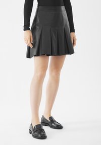 Gonna plissettata in pelle nera con vita alta, texture liscia e forma a A, abbinata a mocassini neri per un look coordinato.