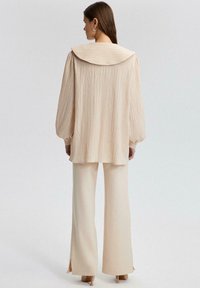 Blusa texturizada beige con un gran cuello, combinada con pantalones de crema de corte acampanado con abertura en los laterales del dobladillo. Tejido suave, ajuste relajado.
