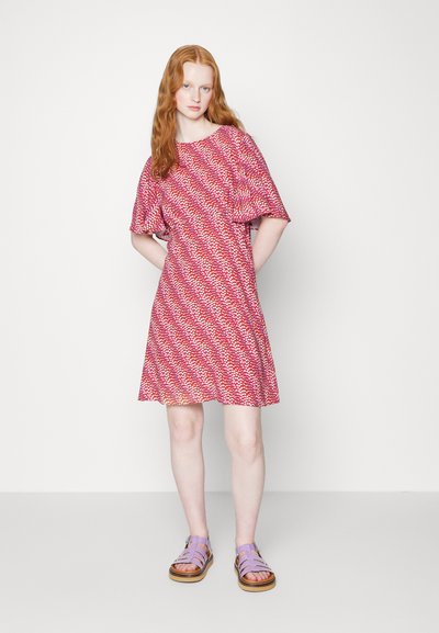 Vestido de manga curta, até ao joelho, em padrão vermelho e branco. Tecido suave com um corte relaxado. Combinado com sandálias lilás claras e solas de madeira.