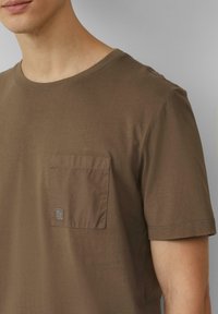 Bruine katoenen t-shirt met een ronde halslijn en een borstzak met een klein logo. Soepele textuur en korte mouwen.