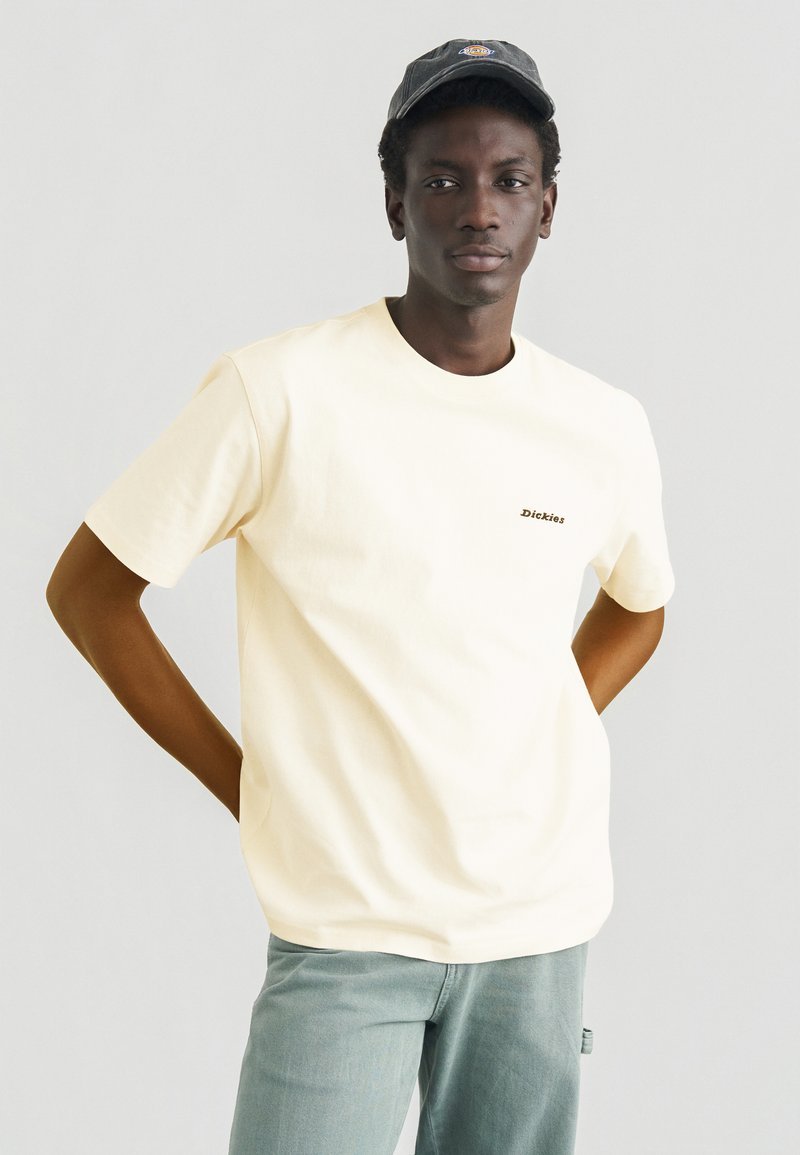 T-shirt in cotone giallo chiaro con maniche corte, scollo rotondo e piccolo logo ricamato. Abbinata a jeans verde chiaro.