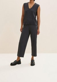 Grå stickad ärmlös topp med V-ringning, i kombination med vida grå byxor. Svarta kraftiga loafers fulländar outfiten. Slät textur.