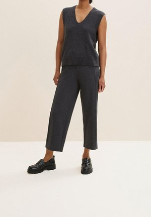 Haut sans manches en tricot gris avec un col en V, associé à un pantalon gris à jambes larges. Des mocassins noirs épais complètent la tenue. Texture lisse.
