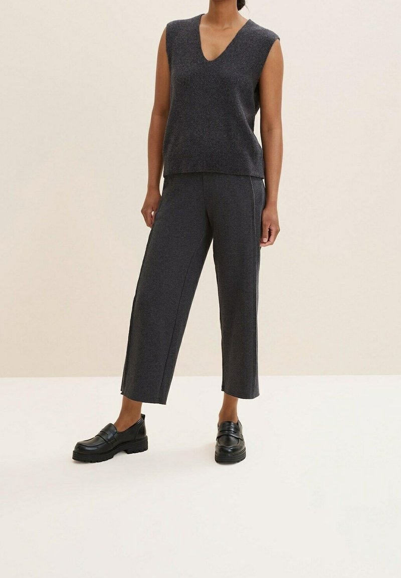 Grå stickad ärmlös topp med V-ringning, i kombination med vida grå byxor. Svarta kraftiga loafers fulländar outfiten. Slät textur.